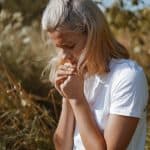 A teenage girl closed her eyes while praying in a field. Hands folded in prayer faith, spirituality and religion concept. Meditation