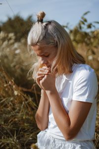 A teenage girl closed her eyes while praying in a field. Hands folded in prayer faith, spirituality and religion concept. Meditation