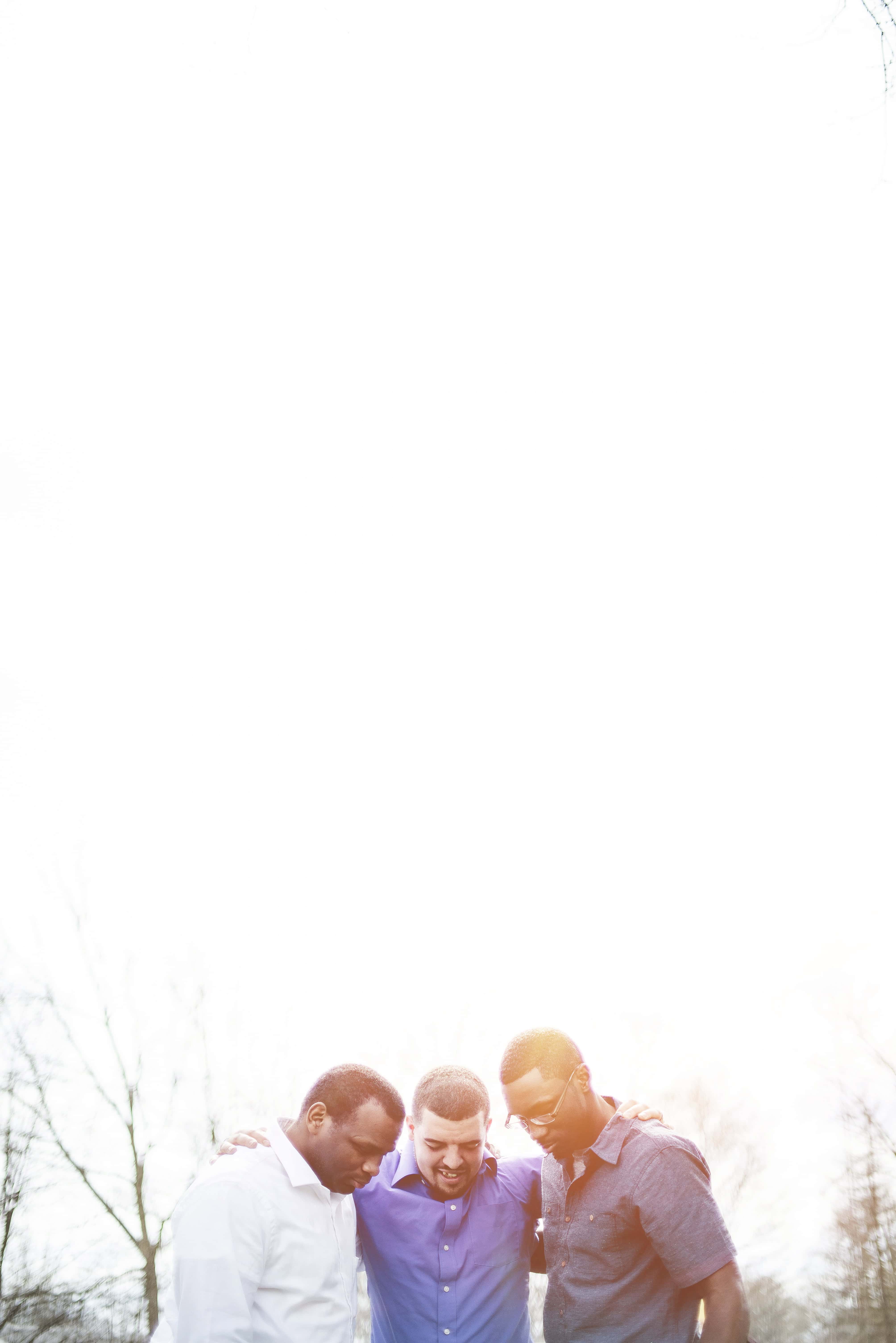A vertical shot of a group of diverse friends standing with hands on shoulders and praying